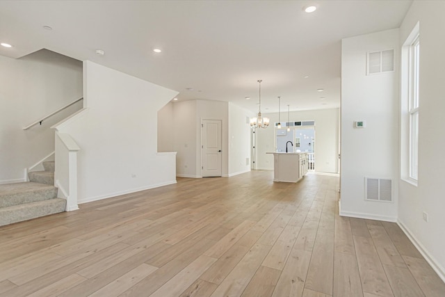 unfurnished living room with visible vents, light wood-style floors, stairway, and a chandelier