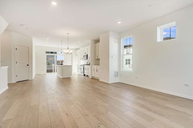 unfurnished living room with a sink, light wood-style flooring, an inviting chandelier, and recessed lighting