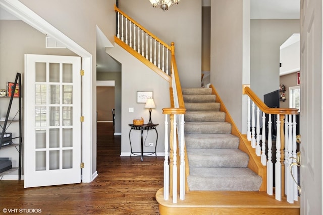 stairway with wood finished floors, an inviting chandelier, baseboards, a high ceiling, and visible vents