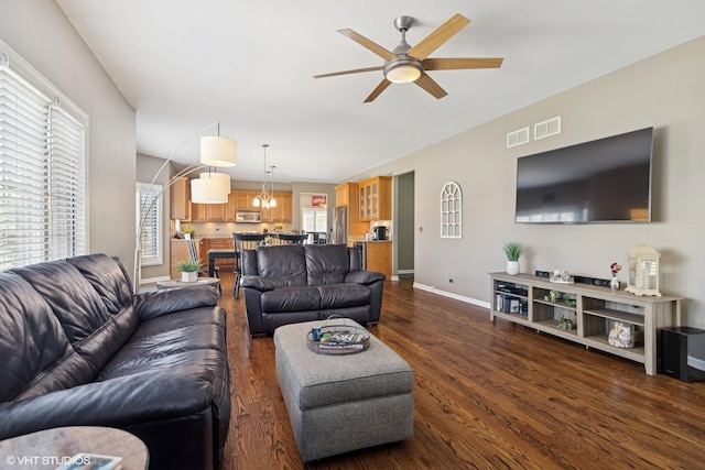 living area featuring baseboards, visible vents, dark wood-style floors, and ceiling fan with notable chandelier