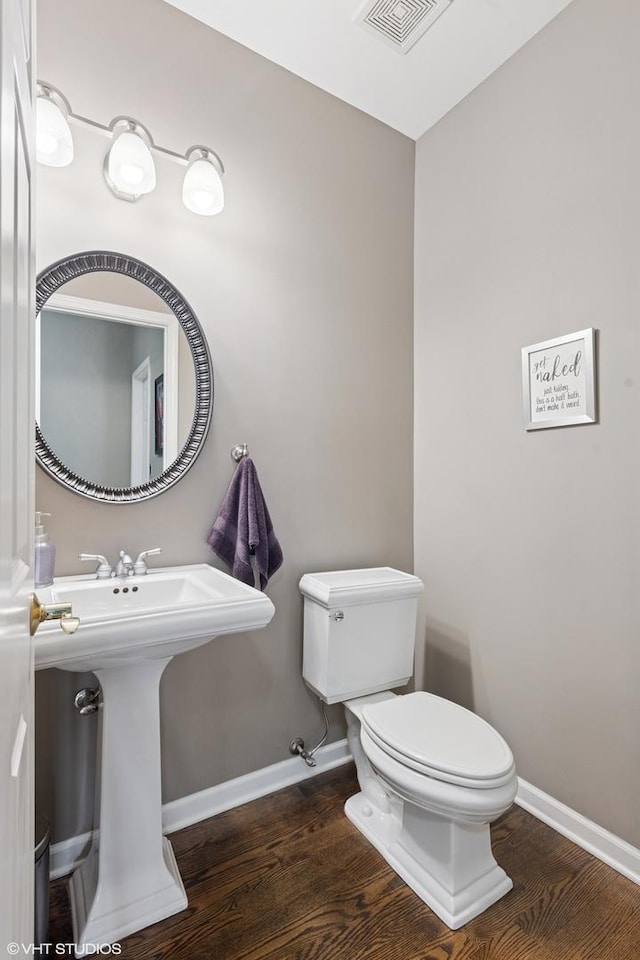 half bathroom with wood finished floors, visible vents, toilet, and baseboards