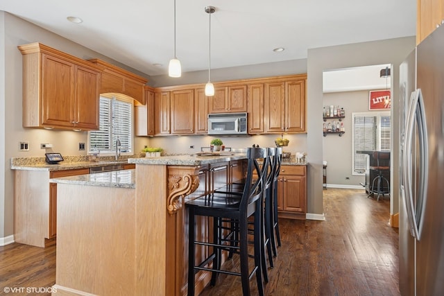 kitchen featuring dark wood finished floors, baseboards, appliances with stainless steel finishes, light stone countertops, and a kitchen island