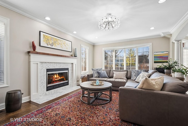 living room with baseboards, ornamental molding, a tiled fireplace, decorative columns, and wood finished floors