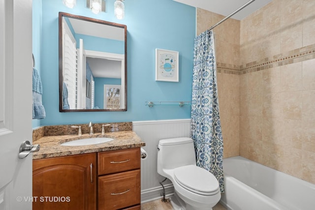 bathroom featuring toilet, shower / bathtub combination with curtain, vanity, and a wainscoted wall