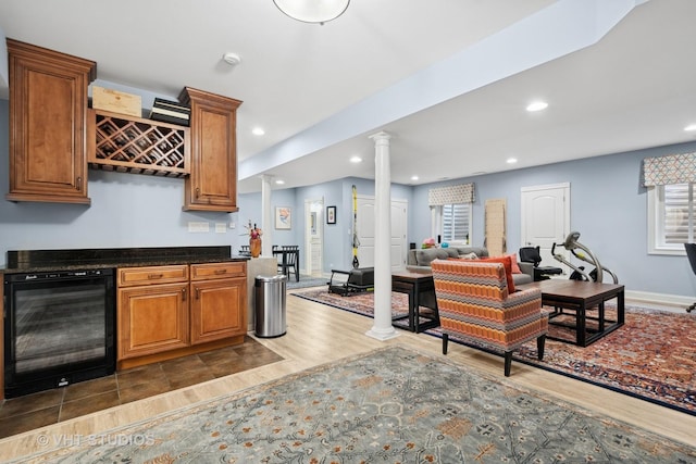 kitchen with wine cooler, brown cabinetry, and decorative columns