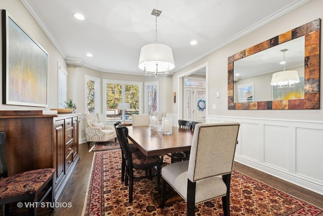 dining area with crown molding, a decorative wall, dark wood-type flooring, a wainscoted wall, and a notable chandelier