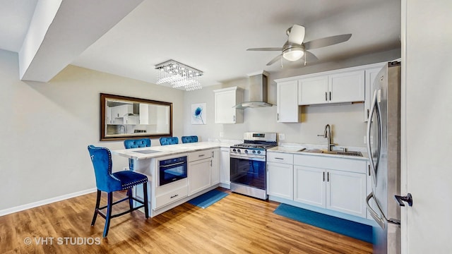 kitchen featuring stainless steel appliances, a peninsula, a sink, white cabinetry, and wall chimney range hood