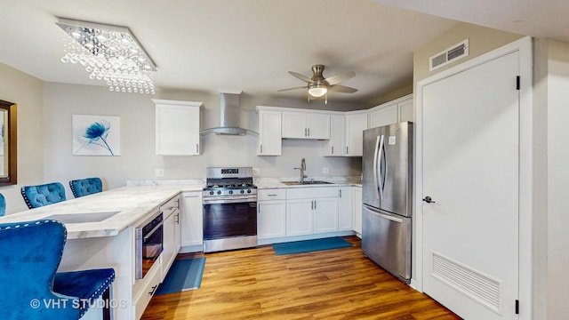 kitchen with visible vents, a sink, wall chimney exhaust hood, a peninsula, and appliances with stainless steel finishes