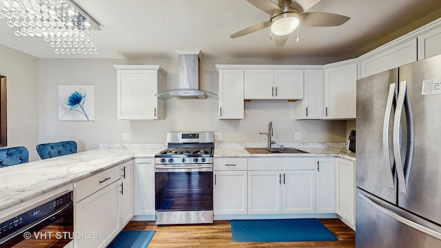 kitchen featuring white cabinets, stainless steel appliances, light wood finished floors, a sink, and wall chimney range hood