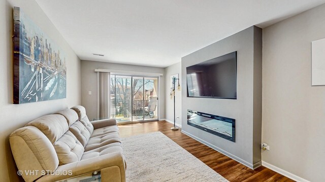 living room with visible vents, a glass covered fireplace, baseboards, and wood finished floors