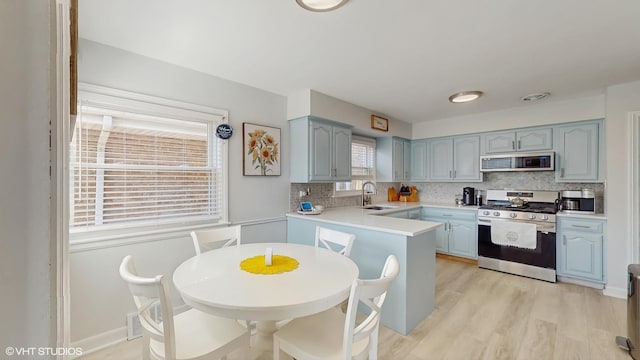 kitchen featuring tasteful backsplash, a peninsula, appliances with stainless steel finishes, light countertops, and a sink