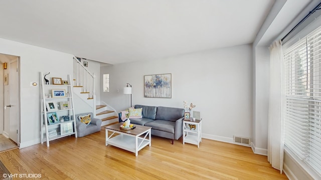 living room featuring visible vents, baseboards, stairway, and light wood-style floors