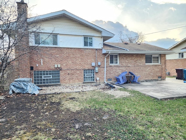 back of house featuring a patio area, roof with shingles, a chimney, brick siding, and a yard