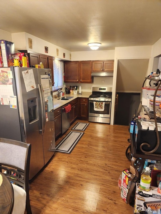 kitchen with light countertops, under cabinet range hood, a sink, light wood finished floors, and appliances with stainless steel finishes