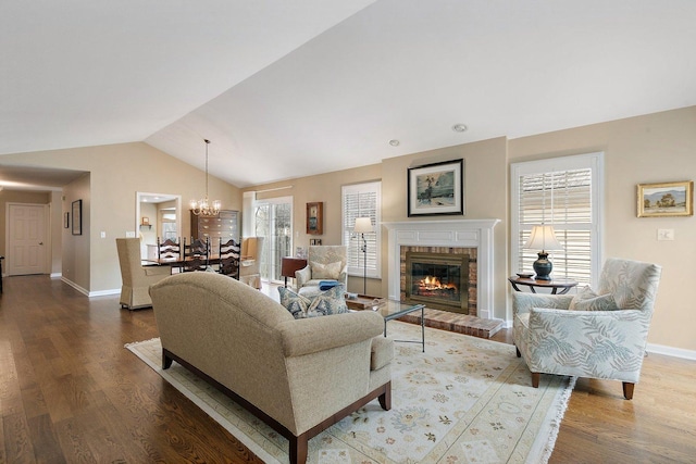 living area with vaulted ceiling, a fireplace, wood finished floors, baseboards, and an inviting chandelier