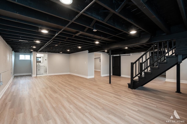 below grade area with stairs, a barn door, wood finished floors, and baseboards