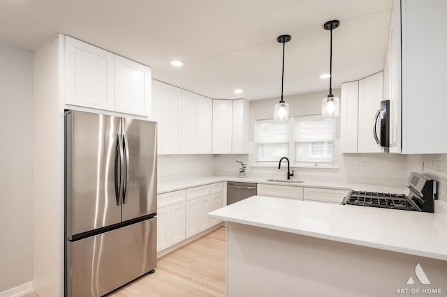 kitchen featuring a sink, light wood finished floors, a peninsula, stainless steel appliances, and decorative backsplash