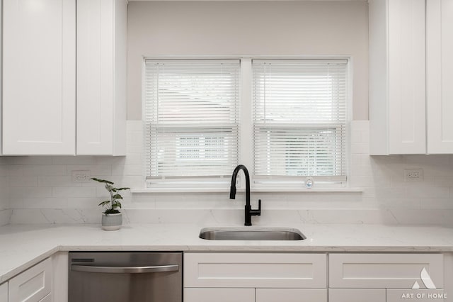 kitchen featuring a sink, light stone countertops, tasteful backsplash, stainless steel dishwasher, and white cabinets