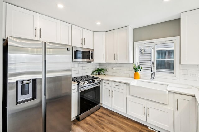 kitchen with a sink, white cabinetry, wood finished floors, stainless steel appliances, and decorative backsplash