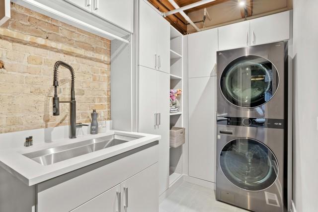 laundry area featuring stacked washer and dryer, a sink, cabinet space, and brick wall