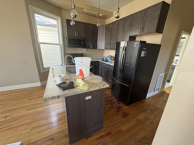 kitchen featuring dark brown cabinetry, freestanding refrigerator, wood finished floors, stainless steel microwave, and baseboards