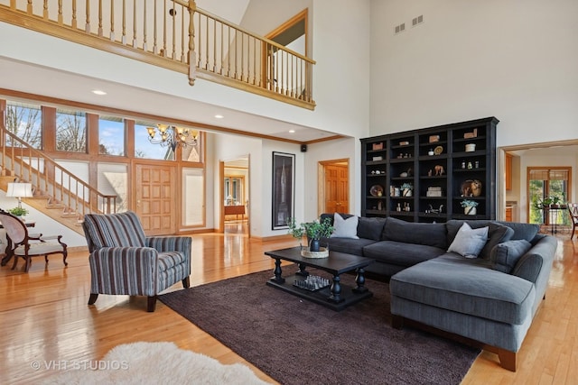 living area with stairway, hardwood / wood-style floors, a towering ceiling, visible vents, and a notable chandelier