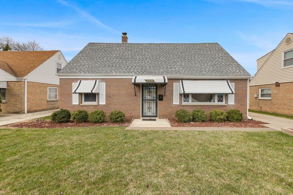 bungalow-style house featuring a shingled roof, a chimney, a front yard, and brick siding