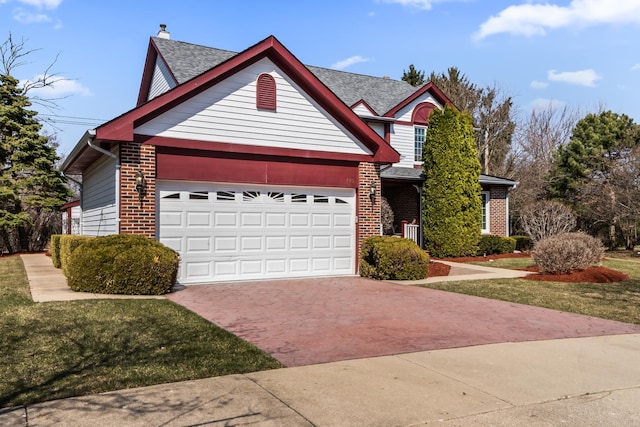 traditional-style home with a chimney, brick siding, an attached garage, a shingled roof, and decorative driveway