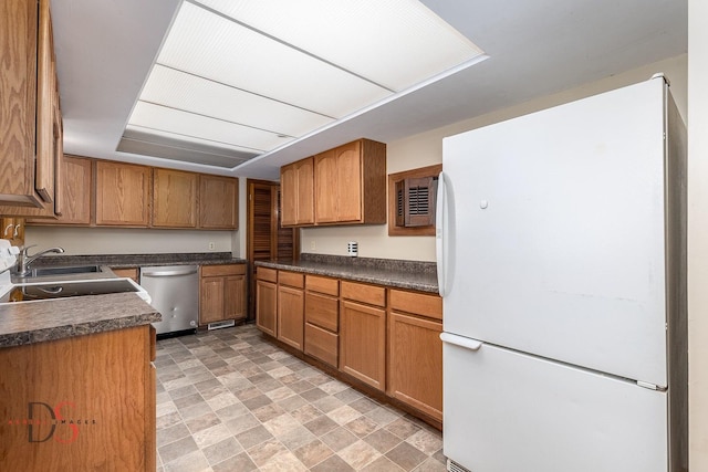 kitchen featuring dishwasher, dark countertops, a sink, brown cabinetry, and freestanding refrigerator