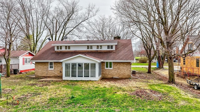 rear view of house featuring a chimney, brick siding, a shingled roof, a sunroom, and a yard