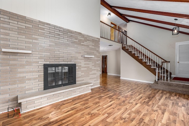 unfurnished living room featuring stairs, a fireplace, wood finished floors, and beam ceiling