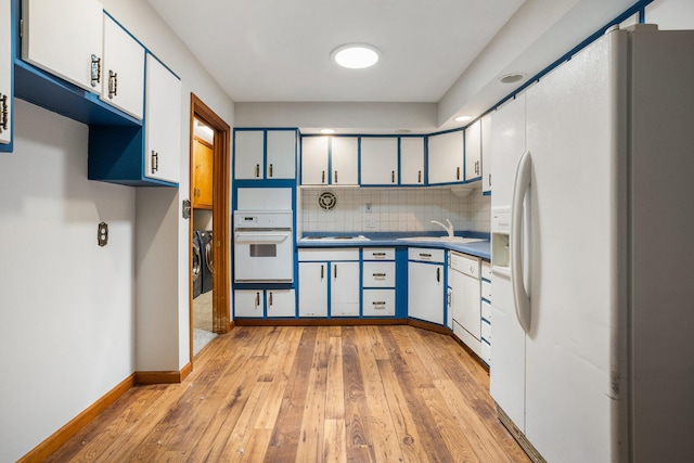 kitchen with tasteful backsplash, white appliances, light wood-style floors, washing machine and clothes dryer, and a sink