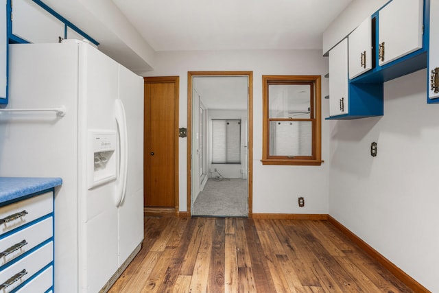 kitchen with blue cabinetry, white refrigerator with ice dispenser, white cabinetry, baseboards, and dark wood finished floors
