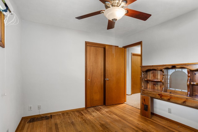 unfurnished bedroom featuring a closet, a ceiling fan, wood finished floors, and baseboards