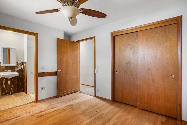 unfurnished bedroom with ceiling fan, baseboards, a closet, wood finished floors, and ensuite bath