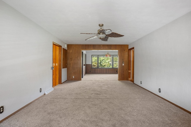empty room with baseboards, wood walls, light carpet, and a ceiling fan