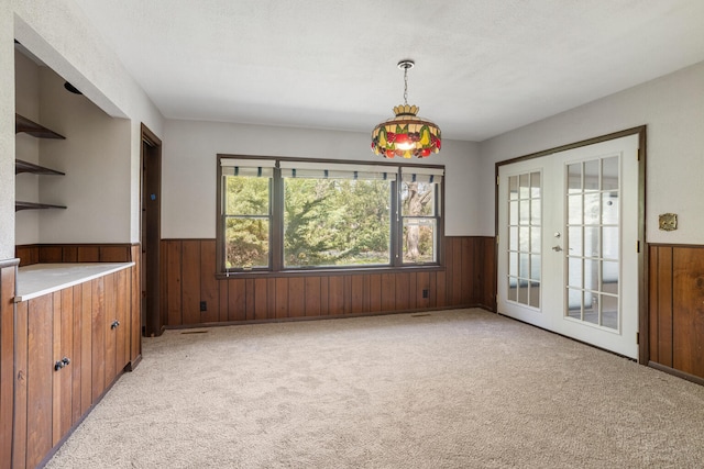 unfurnished dining area with a wainscoted wall, wooden walls, french doors, and light colored carpet
