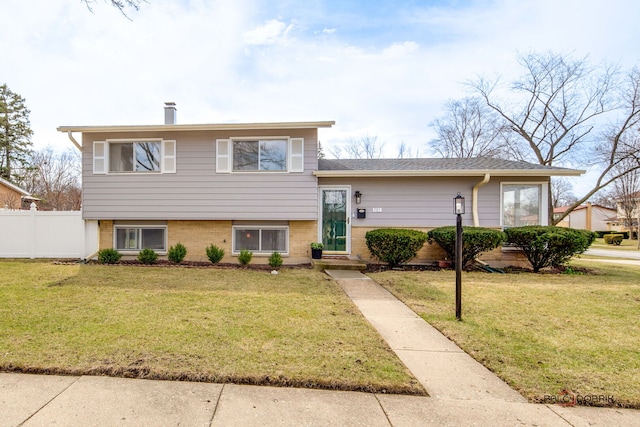 split level home featuring brick siding, a front yard, and fence