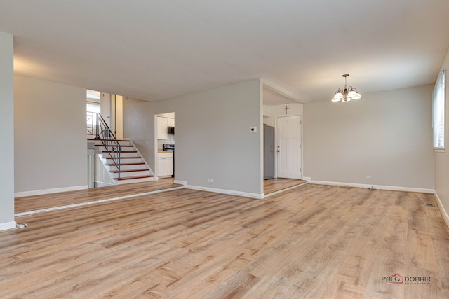 unfurnished living room with stairs, light wood-style floors, baseboards, and an inviting chandelier