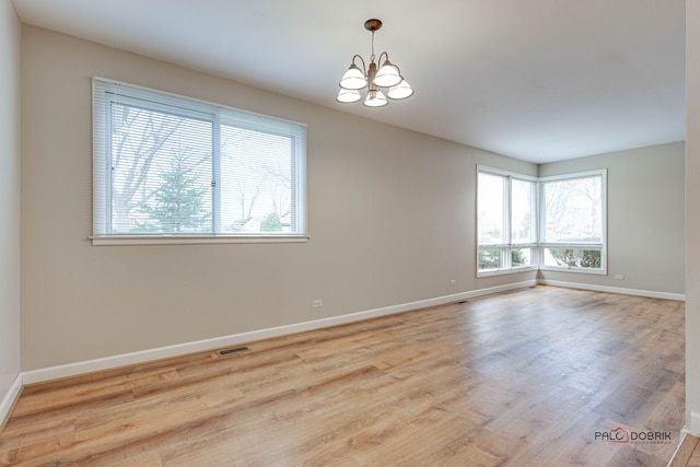 spare room with baseboards, visible vents, a chandelier, and wood finished floors