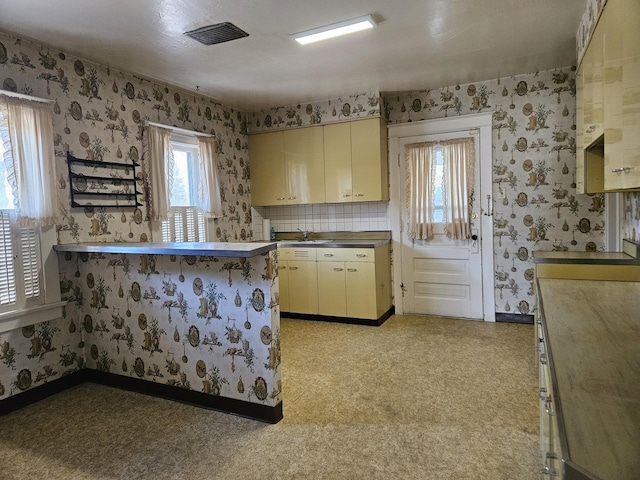 kitchen with a sink, wallpapered walls, cream cabinetry, a peninsula, and visible vents