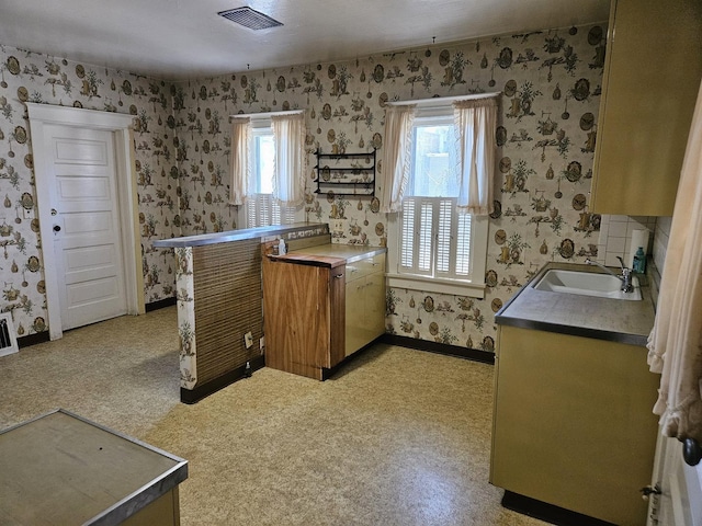 kitchen featuring a sink, baseboards, visible vents, wallpapered walls, and brown cabinets