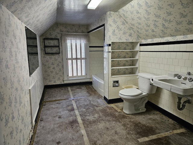 full bath with wallpapered walls, vaulted ceiling, toilet, tile walls, and wainscoting