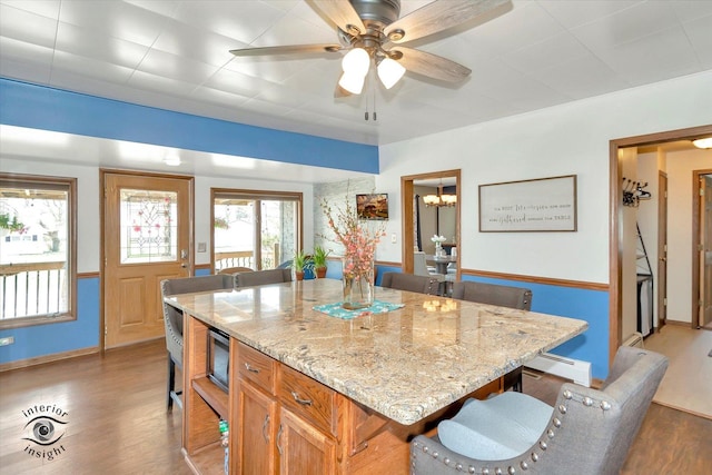 kitchen featuring baseboards, a kitchen bar, wood finished floors, light stone countertops, and a baseboard heating unit