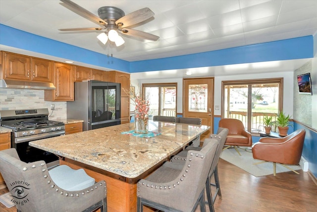 kitchen featuring stainless steel range with gas stovetop, a kitchen bar, under cabinet range hood, light stone counters, and smart refrigerator