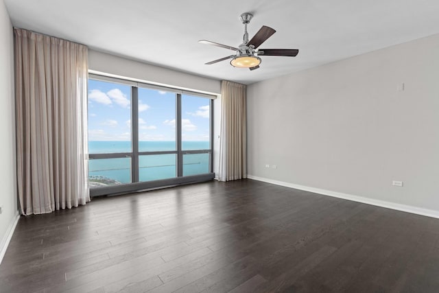 spare room with a water view, dark wood-style floors, baseboards, and a ceiling fan