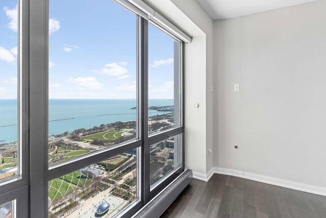 empty room with a water view, dark wood-style flooring, and baseboards