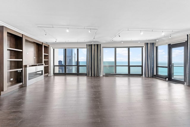 unfurnished living room with built in features, dark wood-style flooring, rail lighting, and a glass covered fireplace