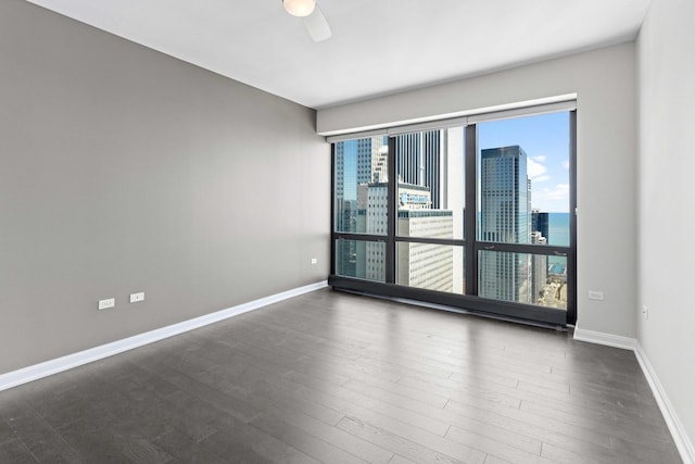 empty room featuring baseboards, a ceiling fan, wood finished floors, and a city view