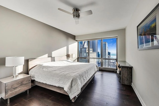bedroom with dark wood-style flooring, baseboards, a ceiling fan, and a view of city